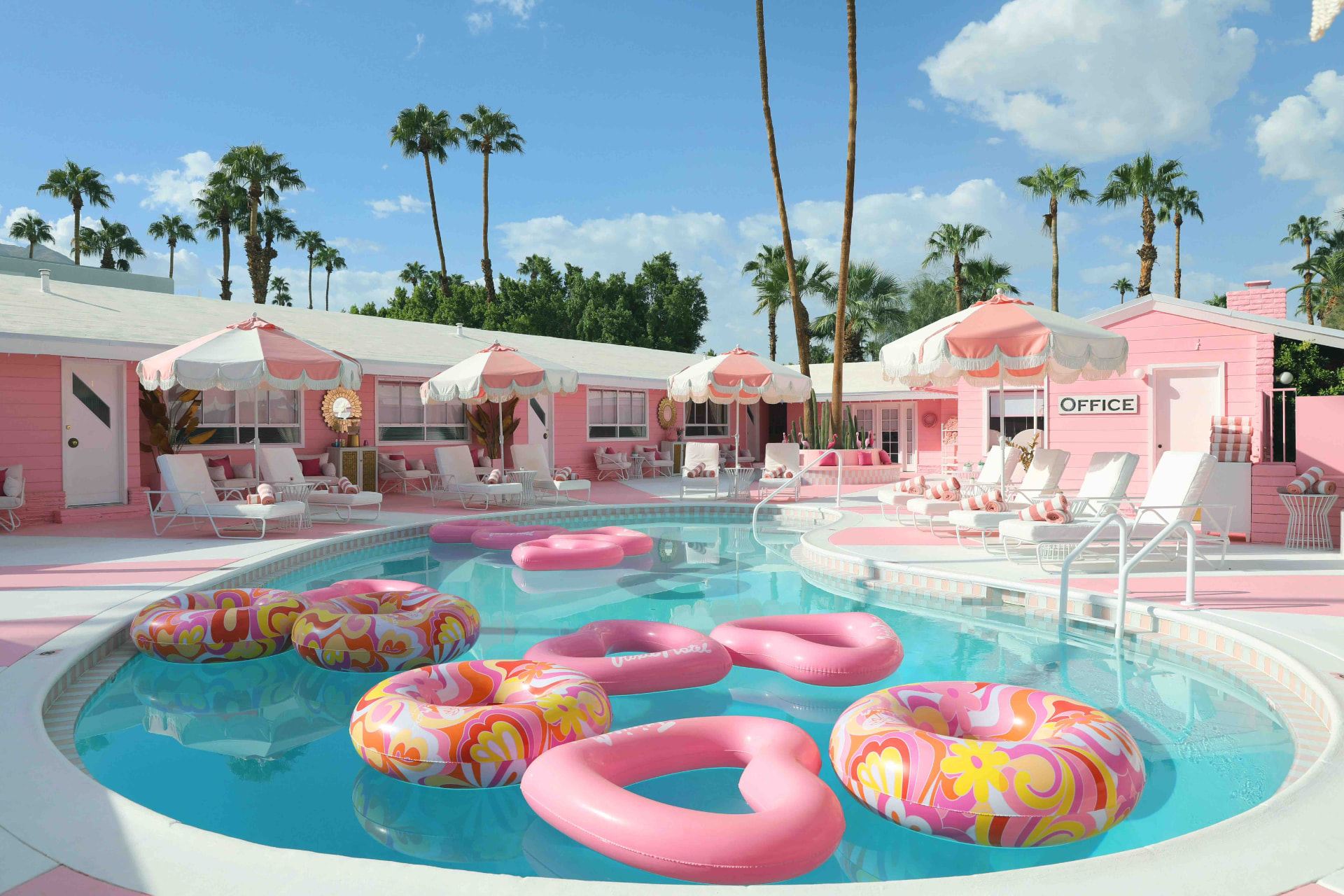 Trixie Motel pink poolside with heart-shaped floats, striped umbrellas and palm trees